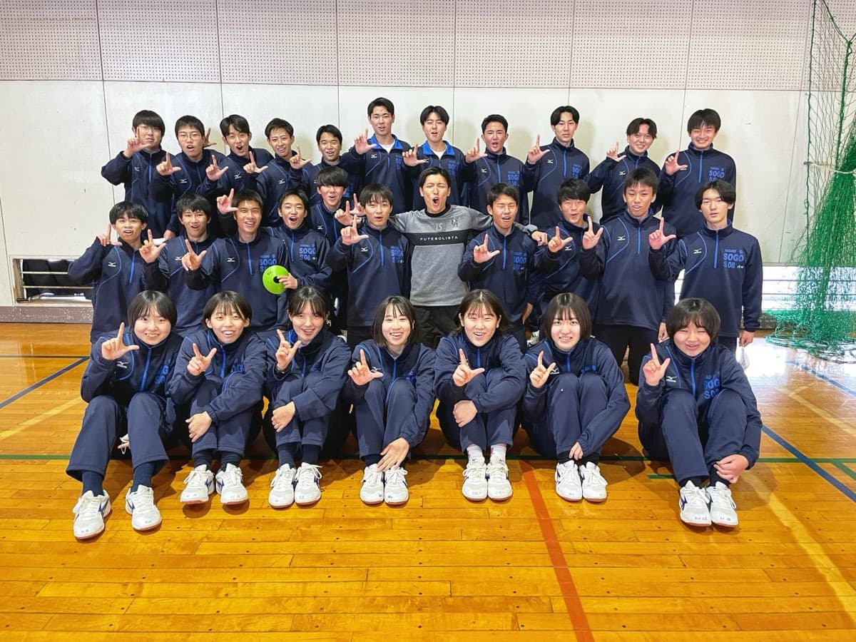 体育館で、生徒と指導者が三列に並んで記念撮影